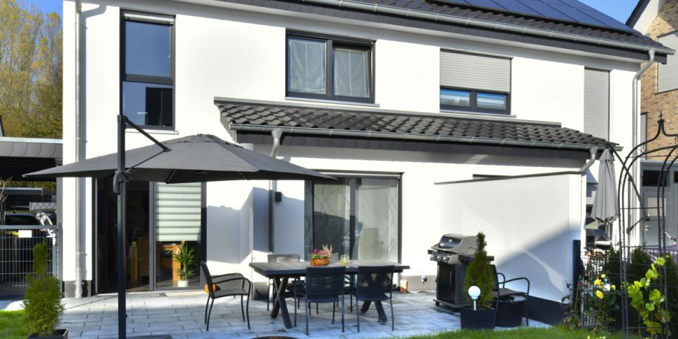 Ein weißes Einfamilienhaus mit schwarzem Dach, auf dem Solarpanel installiert sind.