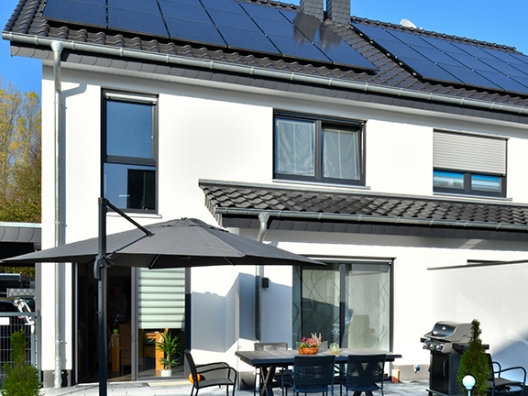 Ein weißes Einfamilienhaus mit schwarzem Dach, auf dem Solarpanel installiert sind.