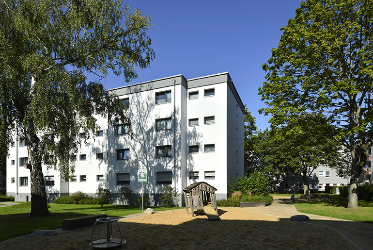 Ein weißes Mehrfamilienhaus mit Flachdach mit Bäumen und einem kleinen Spielplatz