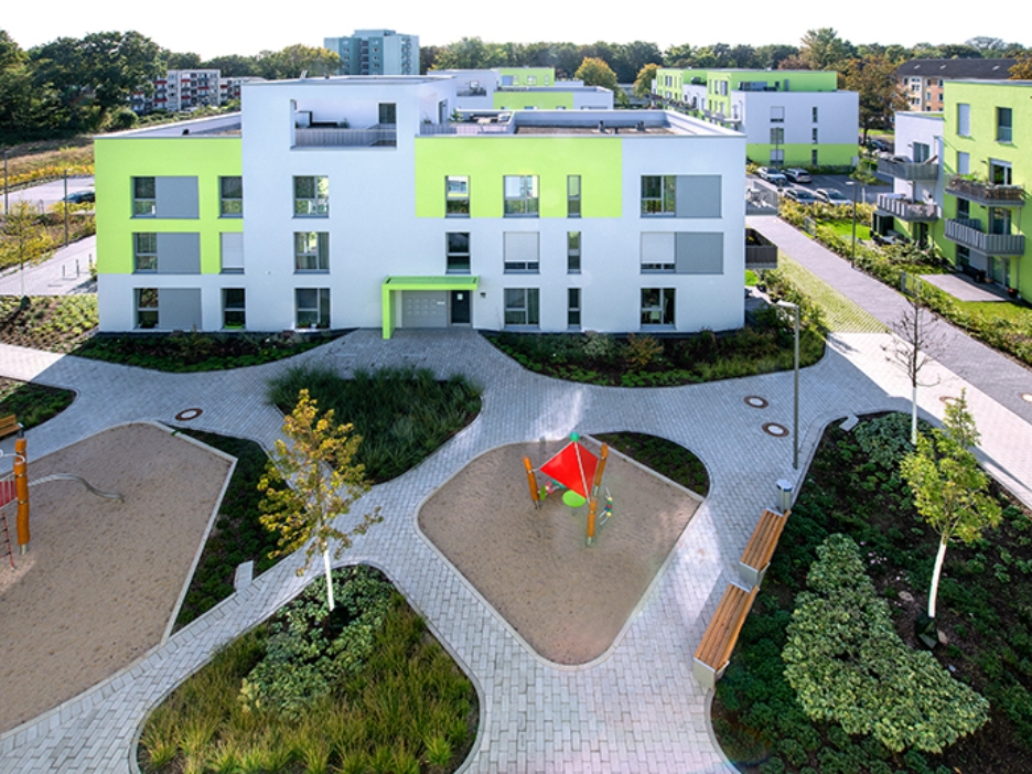 Grün-graue Häuser mit Flachdächern umrahmen einen begrünten Innenhof mit Spielplatz