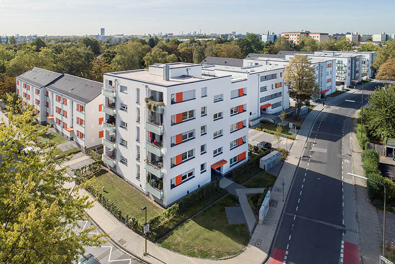 Wohnanlage aus 7 Mehrfamilienhäusern mit Vorgärten und Bäumen im Hintergrund