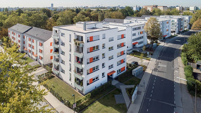 Wohnanlage aus 7 Mehrfamilienhäusern mit Vorgärten und Bäumen im Hintergrund