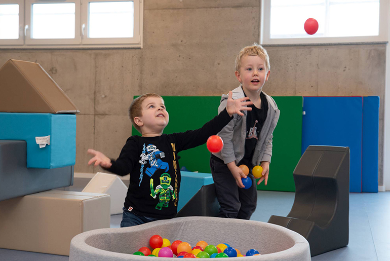 Zwei Kinder spielen mit Bällen aus einem kleinen Bällebad