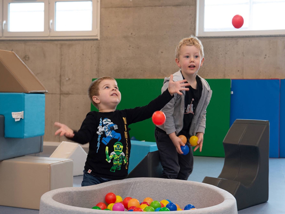 Zwei Kinder spielen mit Bällen aus einem kleinen Bällebad