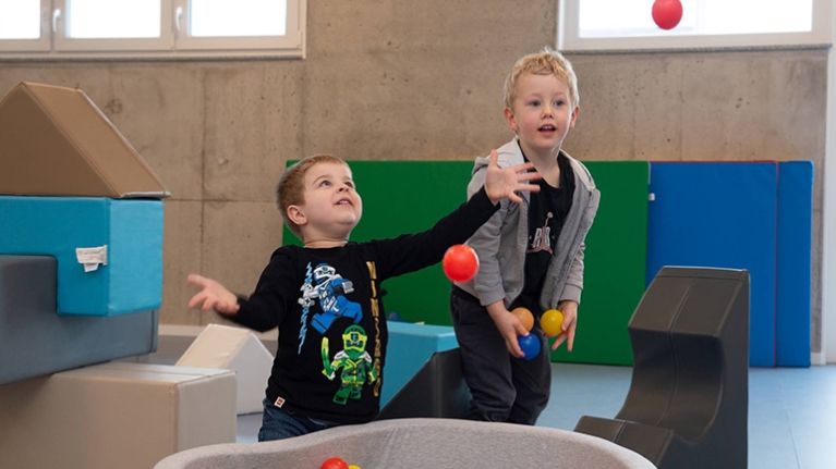 Zwei Kinder spielen mit Bällen aus einem kleinen Bällebad