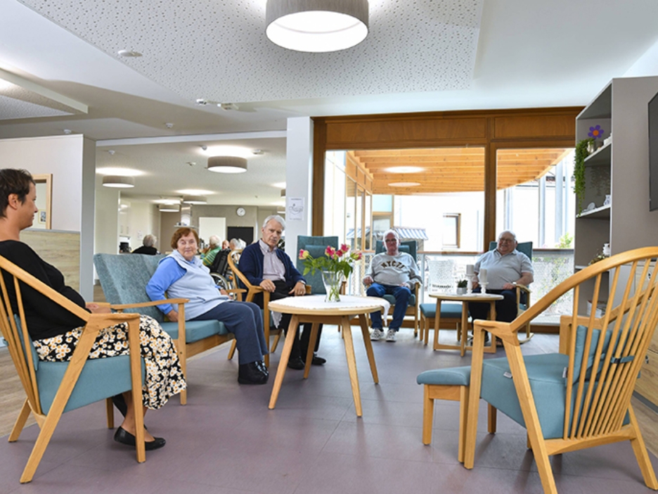 Alte Menschen sitzen in einer Holz-Sitzgruppe mit türkisen Polstern.