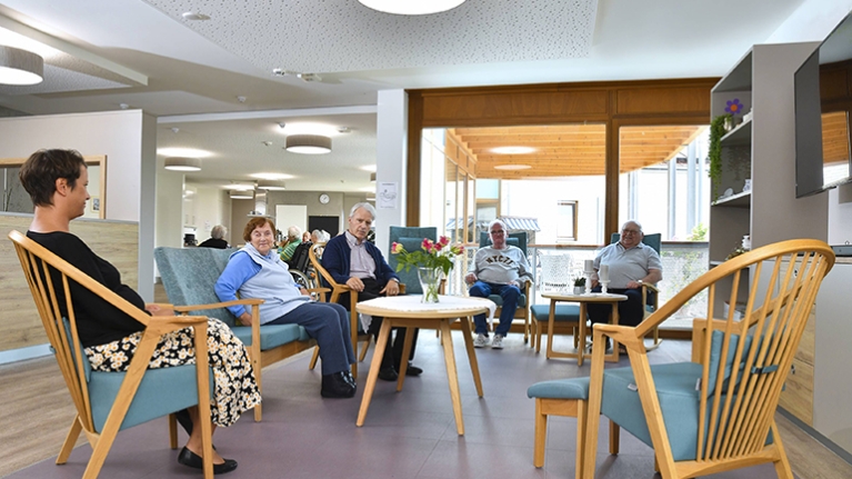 Alte Menschen sitzen in einer Holz-Sitzgruppe mit türkisen Polstern.