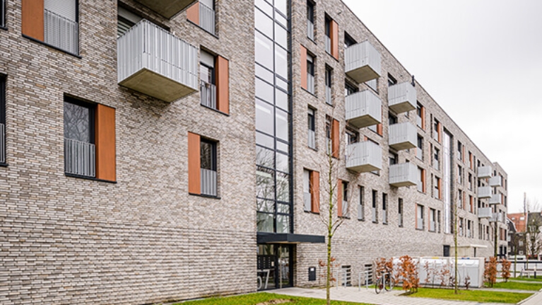 Hausfront einer modernen Wohnanlage mit Vorgärten und Fahrradständer am Eingang