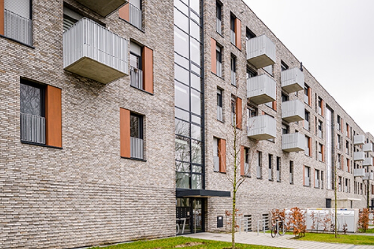 Hausfront einer modernen Wohnanlage mit Vorgärten und Fahrradständer am Eingang