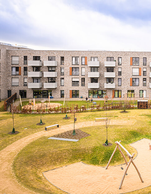 Hausfront einer modernen Wohnanlage, davor eine große Grünfläche mit Spielplatz