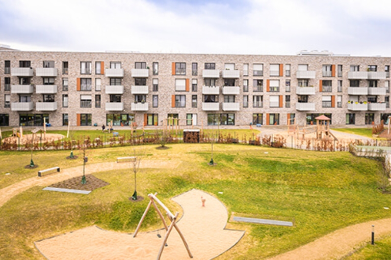 Hausfront einer modernen Wohnanlage, davor eine große Grünfläche mit Spielplatz