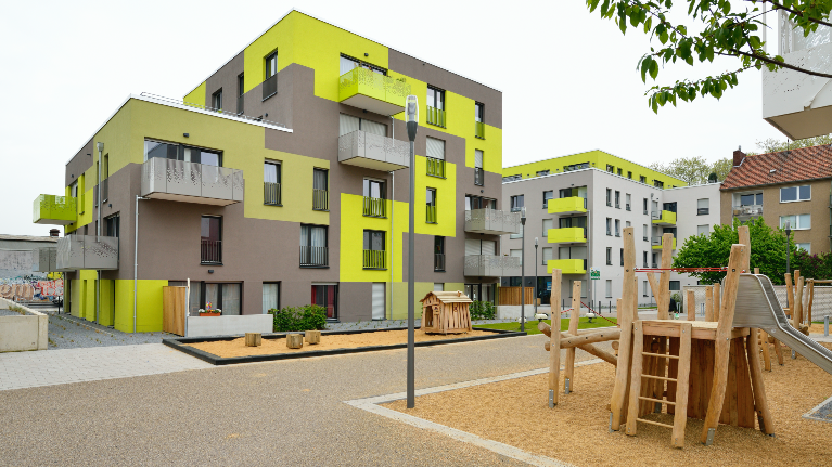 Modernes Wohnquartier mit gelb-grauer Fassade, davor ein Spielplatz