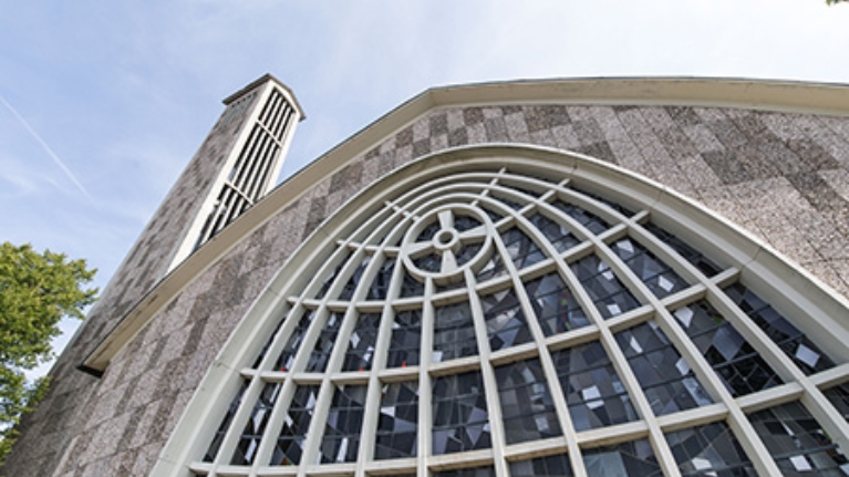 Graue Stein-Fassade einer Kirche mit geschwungener Fensterfront aus der Froschperspektive
