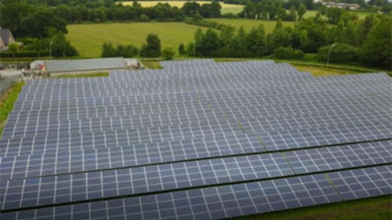 Großflächige Solaranlage auf einer Wiese. Im Hintergrund Felder und Bäume