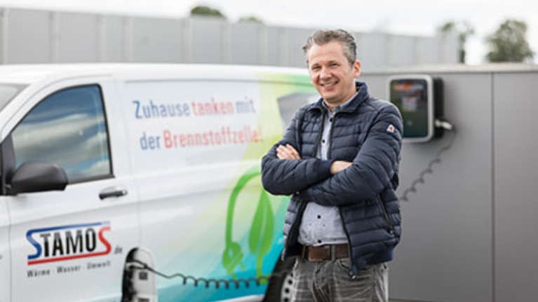 Ein Mann vor einem Elektro-Lieferwagen der Firma Stamos. Dieser wird gerade geladen.