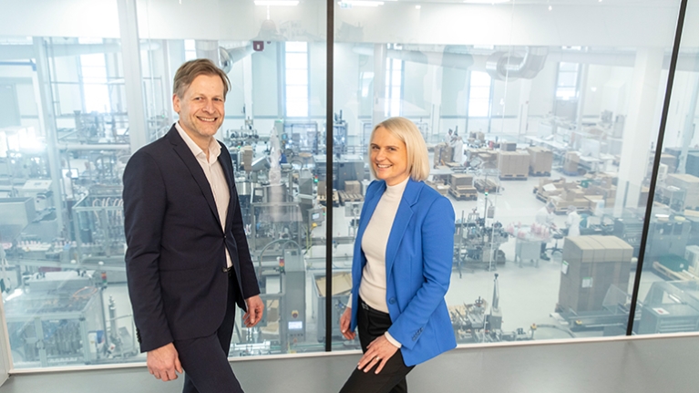 Babor-Geschäftsführer Stefan Kehr war Claudia Brendt von der Förderberatung Rheinland stehen vor einer scheibe, die den Produktionsbereich abtrennt