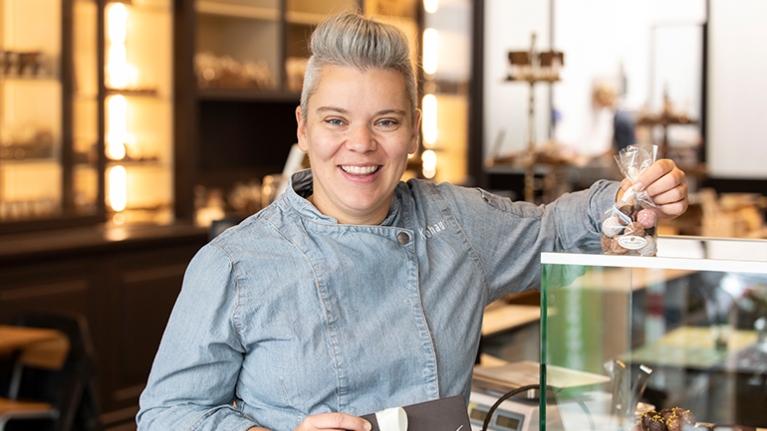 Die junge Konditorin Lathrin Lohaus steht in ihrem Cafe mit einer Packung Pralinen neben dem Tresen.