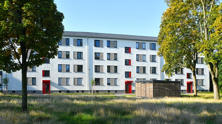 Ein großflächiges Mietshaus mit weißer Fassade und roten Türelementen im Grünen