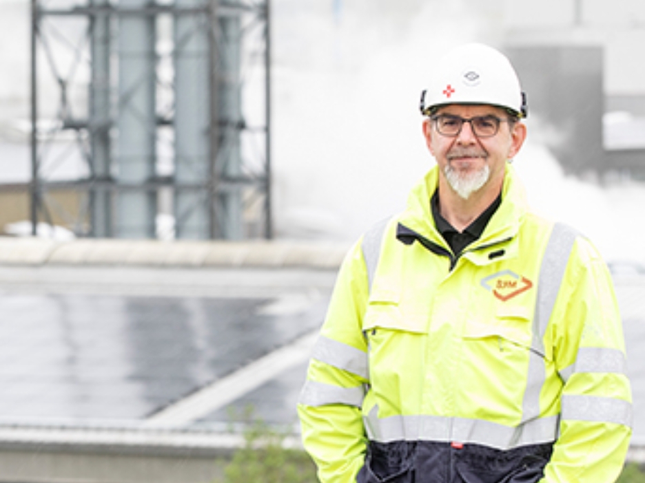 Andreas Fedderwitz, Elektroingenieur bei dem Recyclingbetrieb, steht in gelber Warnjacke auf einer Anhöhe vor den Fabrikdächern mit Solarmodulen