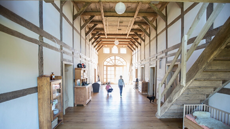 Innenraum einer zu einer Kita umgebauten Kirche mit Holzdielen und -balken. 2 Kinder spielen mit einer Katze.