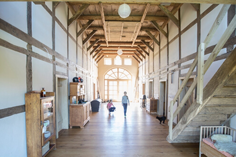 Innenraum einer zu einer Kita umgebauten Kirche mit Holzdielen und -balken. 2 Kinder spielen mit einer Katze.