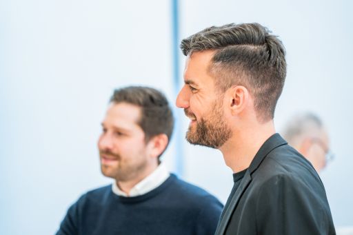 Zwei Männer im Gespräch, einer im Vordergrund im Profil, beide lächeln.